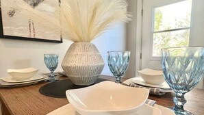 Een eettafel gedekt met witte borden, blauw servies en een vaas met witte veertjes.
