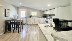Una cocina amplia con una isla central, armarios blancos y una cafetera negra.