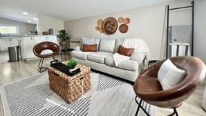 Una sala moderna con un sofá, dos sillones, una mesita de centro y decoración en la pared.