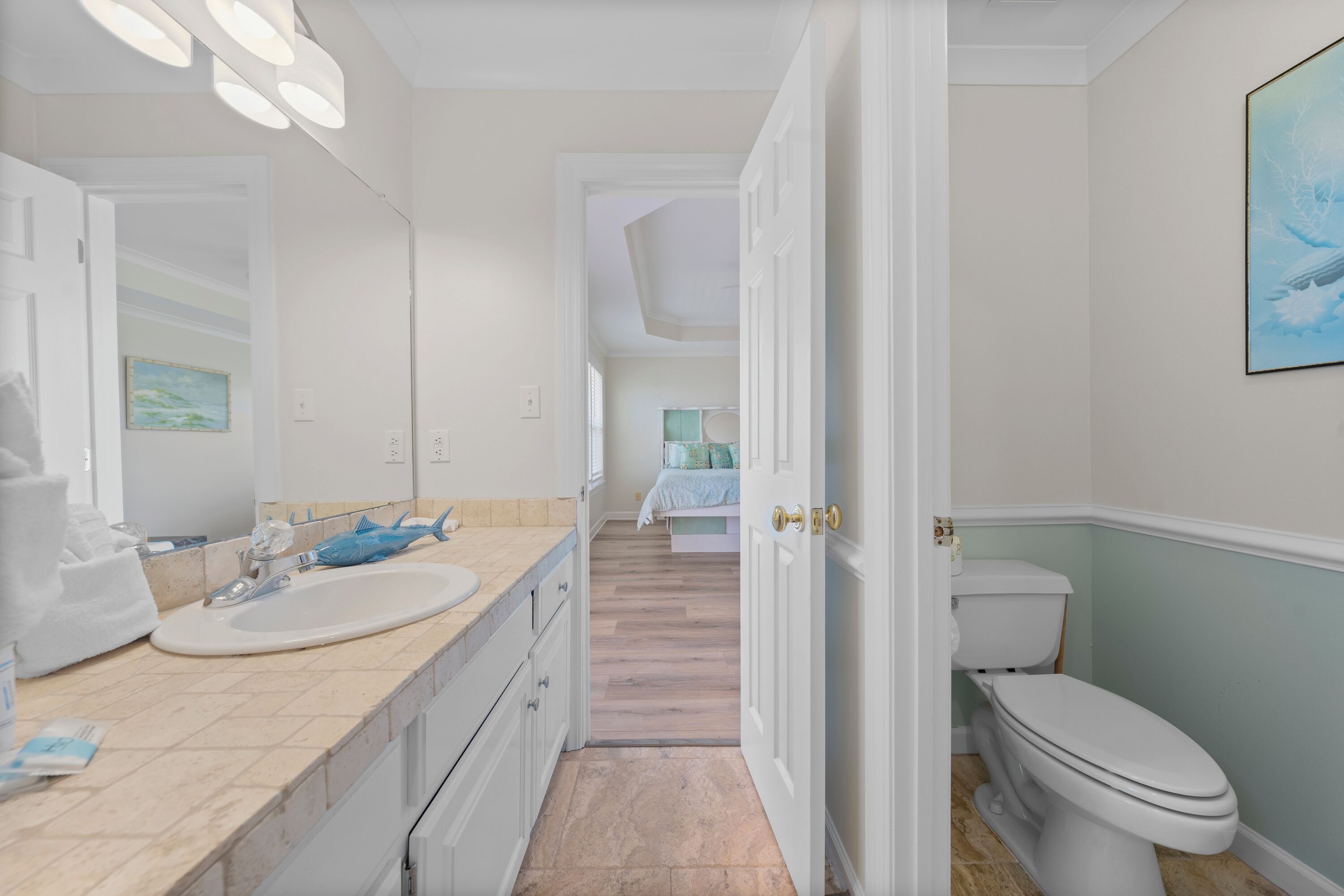 A bathroom with a sink, mirror, and toilet. There is a door leading to another room.