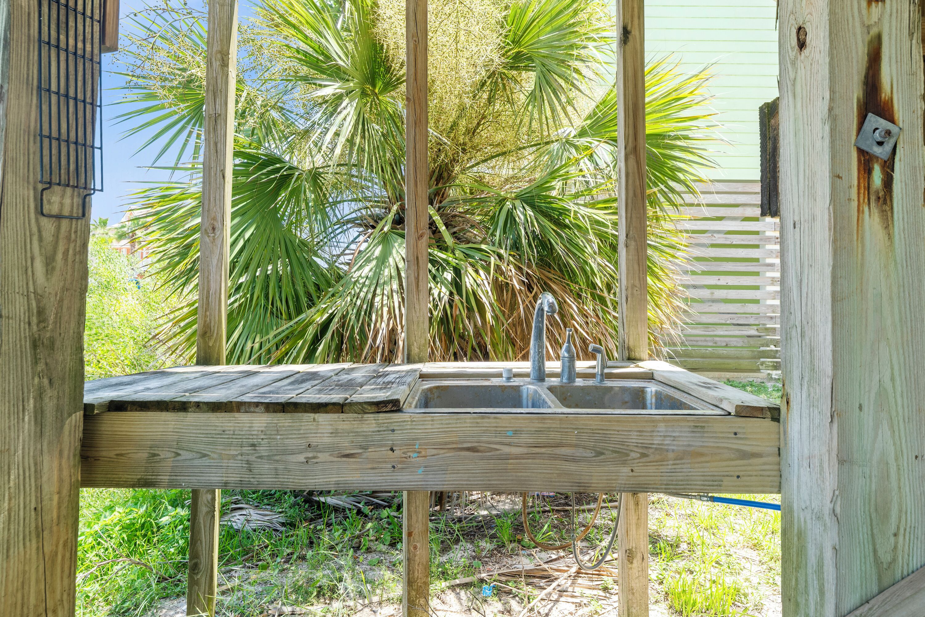 A wooden outdoor sink area with a metal faucet, surrounded by wooden beams and palm trees.