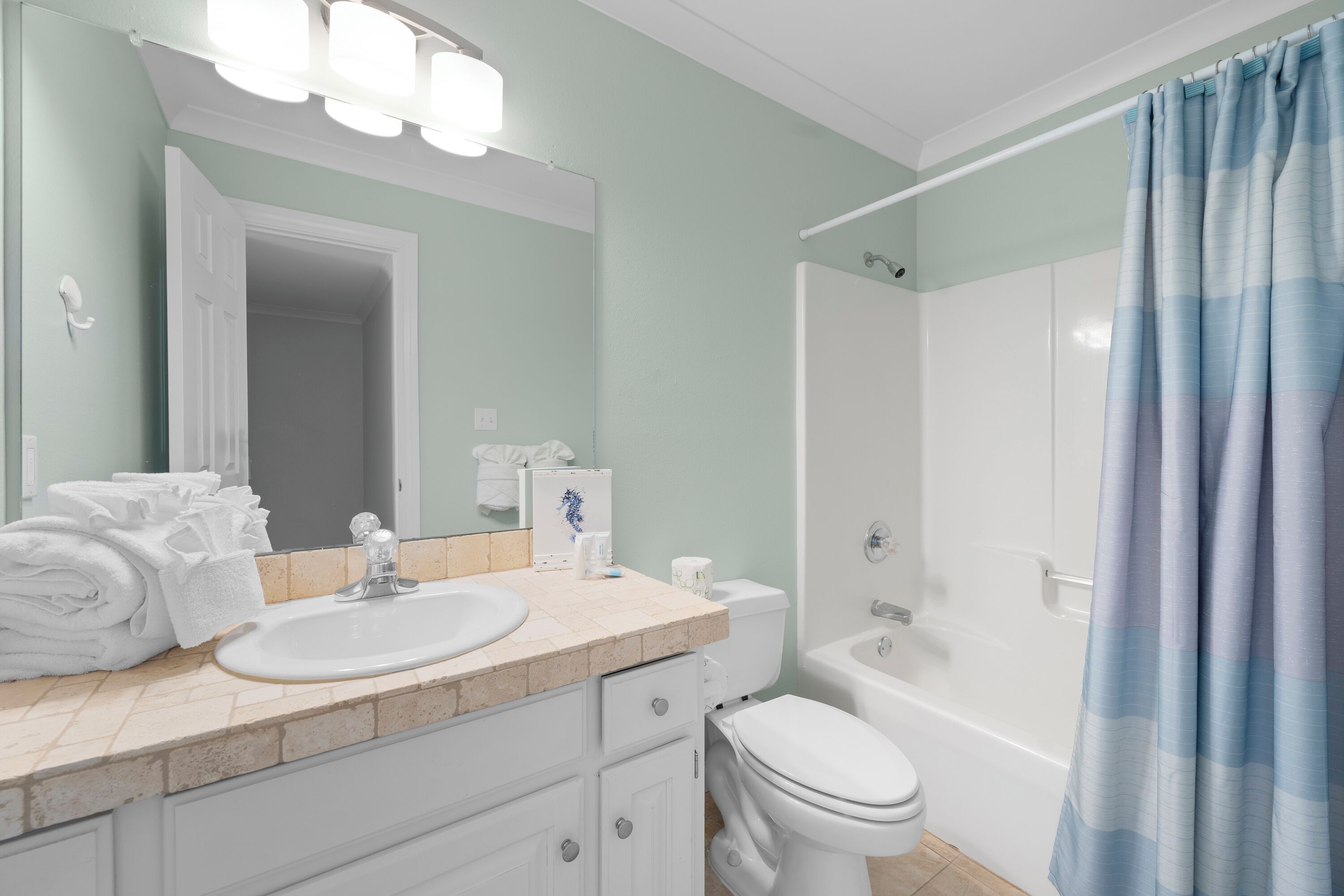 Une salle de bain avec un lavabo, des toilettes et une douche. Des serviettes sont pliées et empilées sur le comptoir.