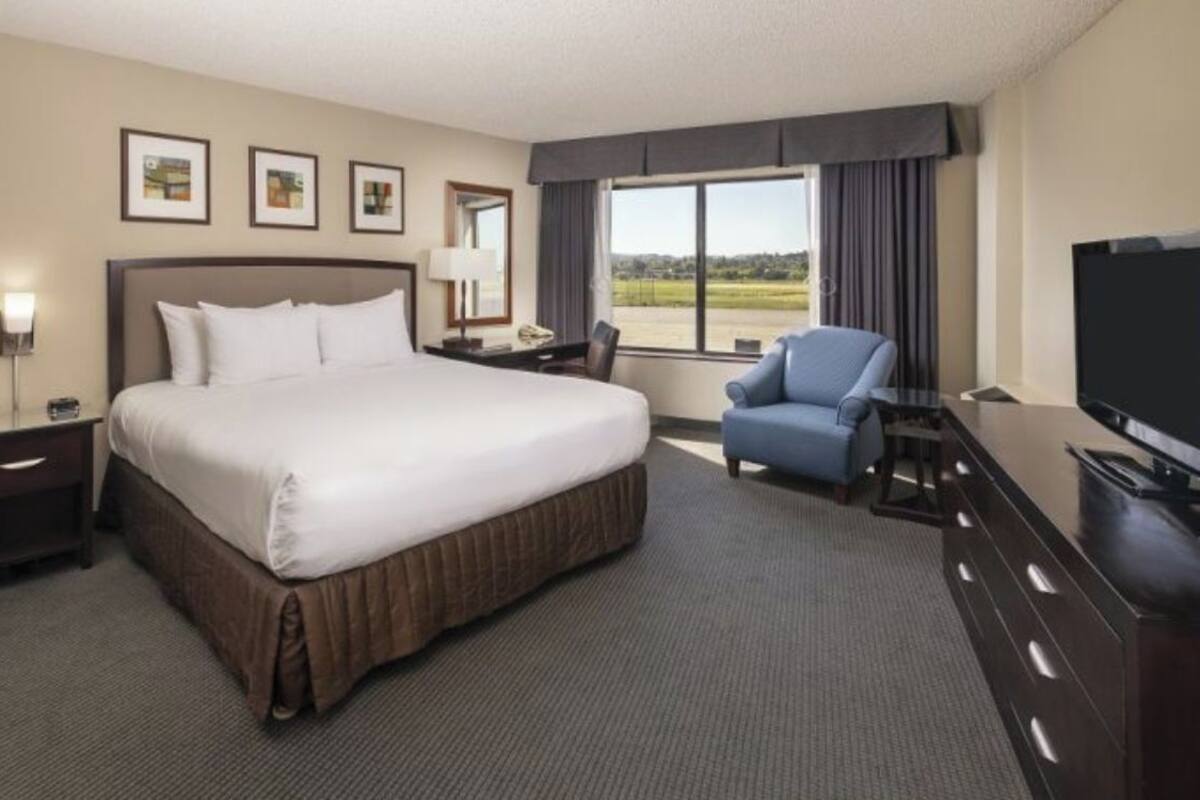 Une chambre d’hôtel avec un grand lit, un bureau avec une chaise, une télévision et une fenêtre donnant sur un beau paysage.