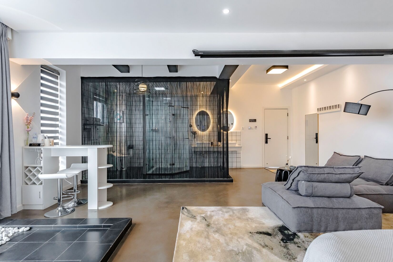 A modern living room with a grey sofa, a white coffee table, and a glass partition with circular lights.