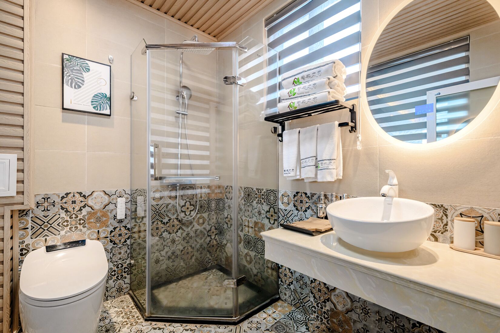 Un baño con ducha de vidrio, un lavamanos amplio con espejo y azulejos estampados.