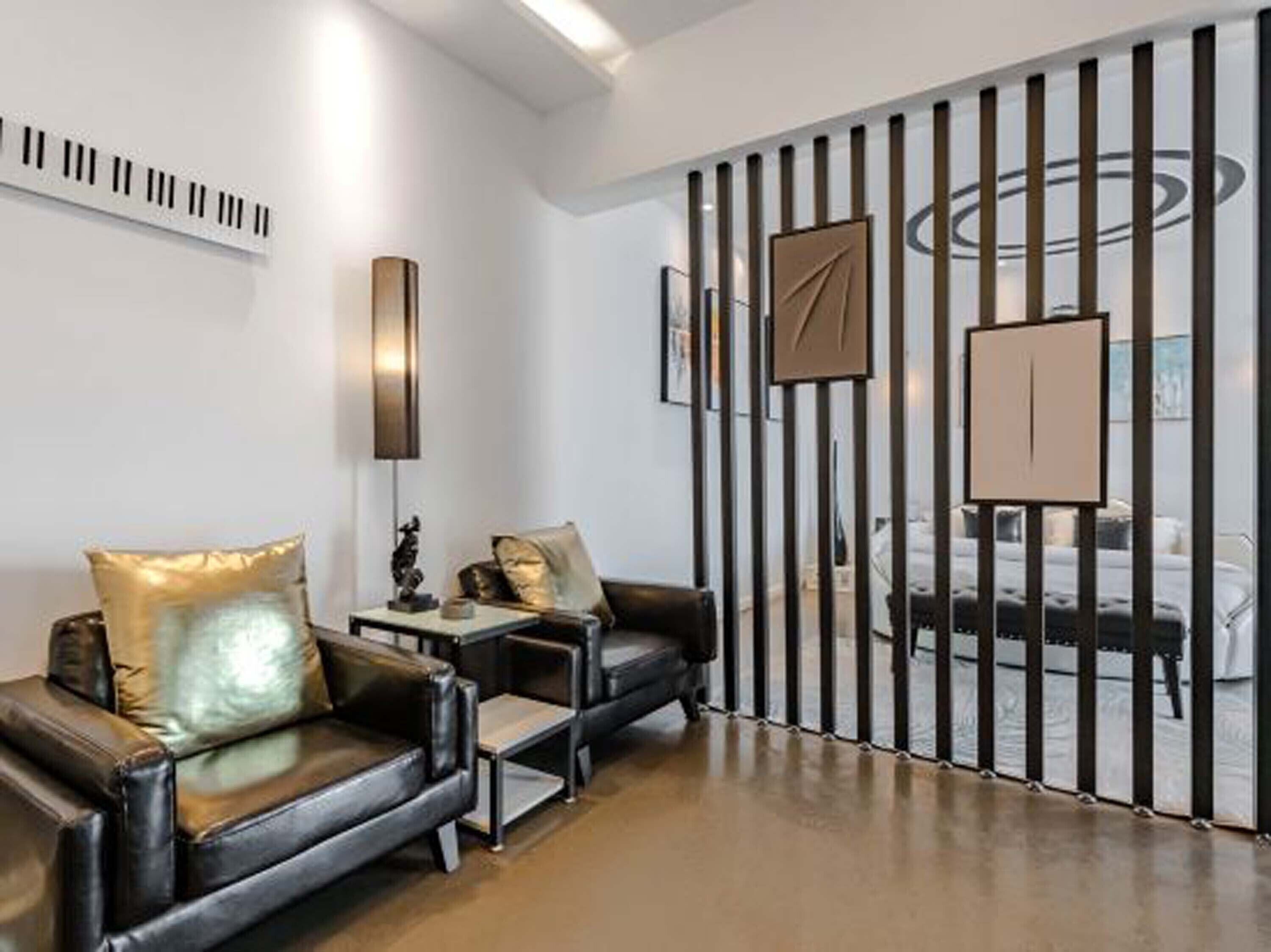 Un saló modern amb un sofà de cuir negre, una taula auxiliar petita i un panell decoratiu a la paret.