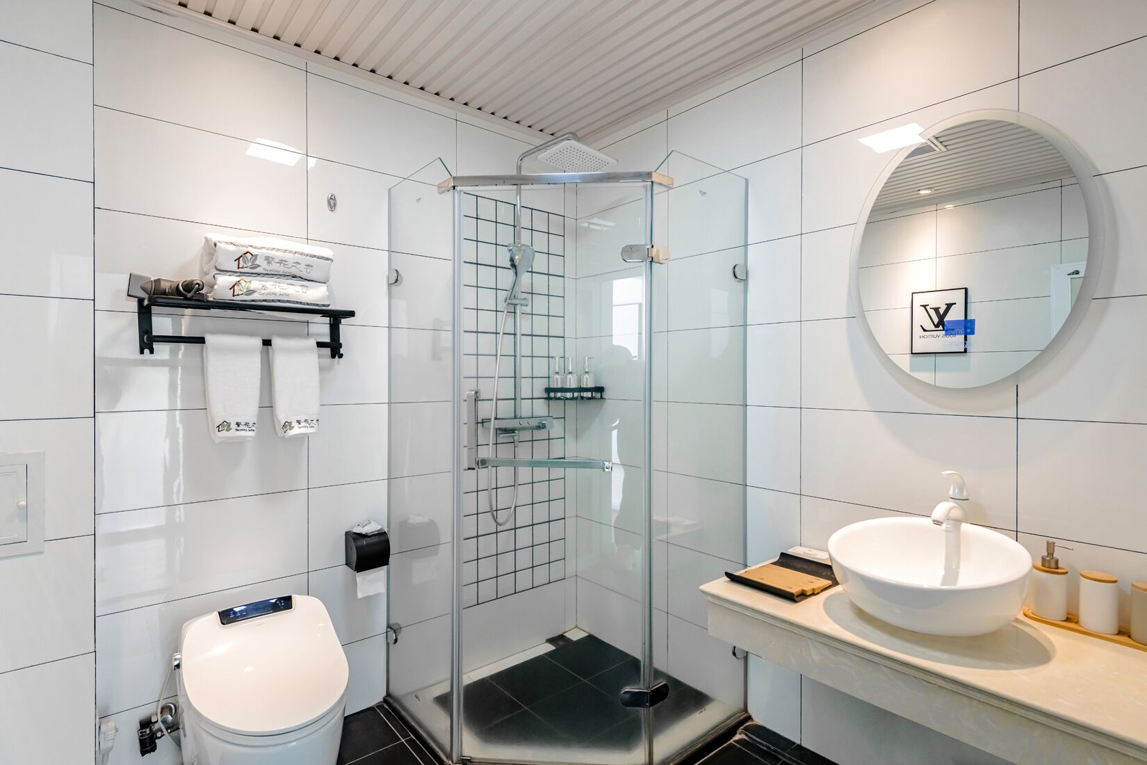A modern bathroom with a glass-enclosed shower, a white sink with a round mirror, and a toilet.