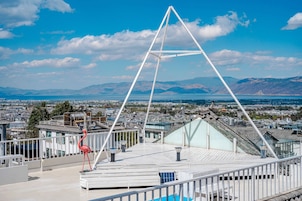A rooftop terrace with a white metal structure, a red flamingo sculpture, and a view of a cityscape with mountains in the background.