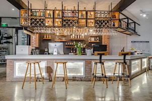 A bar area with a brick wall, wooden stools, and a variety of bottles and glasses on shelves.