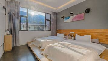 A hotel room with two beds, a wooden headboard, a large window with a view of mountains, and a painting on the wall.