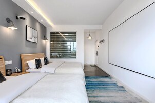 Una habitación de hotel moderna con dos camas, un ventanal con persianas, un tapete azul y un diseño minimalista.