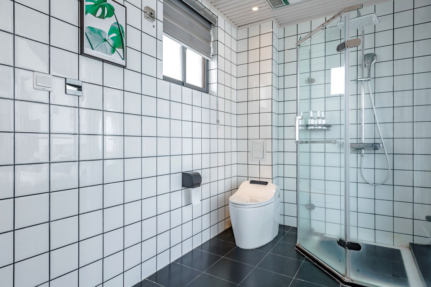Un baño moderno con paredes de azulejos blancos, suelo negro, inodoro y cabina de ducha de vidrio.