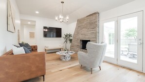 A modern living room with a fireplace, a sofa, a coffee table, and a TV mounted on the wall. - The Abbey at Lake Hefner (The Village)