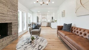 A spacious living room with a fireplace, a marble coffee table, a leather sofa, and a modern chandelier. - The Abbey at Lake Hefner (The Village)