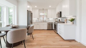 A modern kitchen with white cabinets, a central island, and a dining area with chairs. - The Abbey at Lake Hefner (The Village)