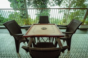 A table with a board game, surrounded by chairs, on a balcony with a railing and potted plants. - 3-Bedroom Villa in Paithalmala with Spacious Open Kitchen and Enchanting Canopy (Naduvil)