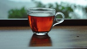 A clear glass cup of tea on a wooden surface with a blurred view of greenery and mountains in the background.
