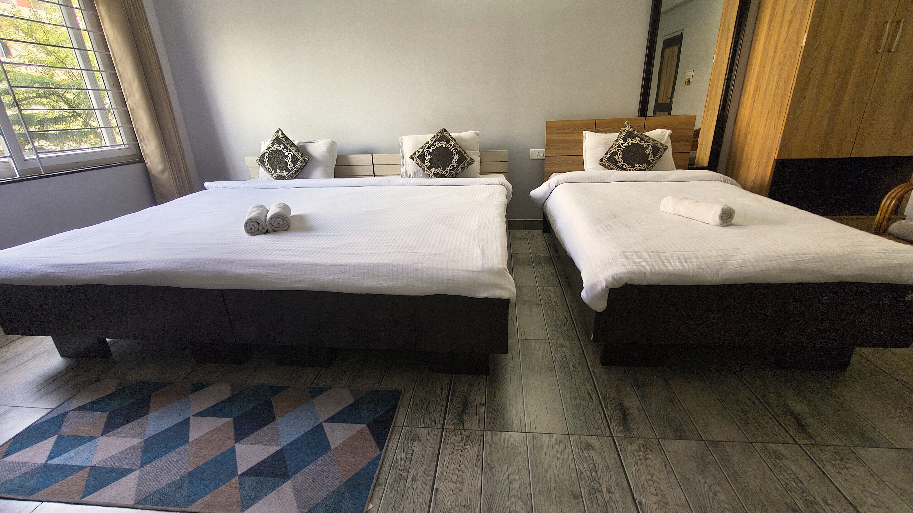 Een hotelkamer met twee bedden, een kamerkleed met patroon en een raam met zonwering.