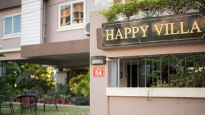 Une enseigne indiquant « HAPPY VILLA » au-dessus de l’entrée d’un immeuble, avec une petite fenêtre et un bouton de sonnette juste au-dessus.