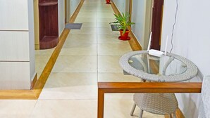 Un couloir d’hôtel avec un sol carrelé, des plantes en pot et un fauteuil en osier.