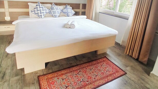 Un lit bien fait, agrémenté d’oreillers à motifs, un tapis rouge et une fenêtre avec des rideaux.
