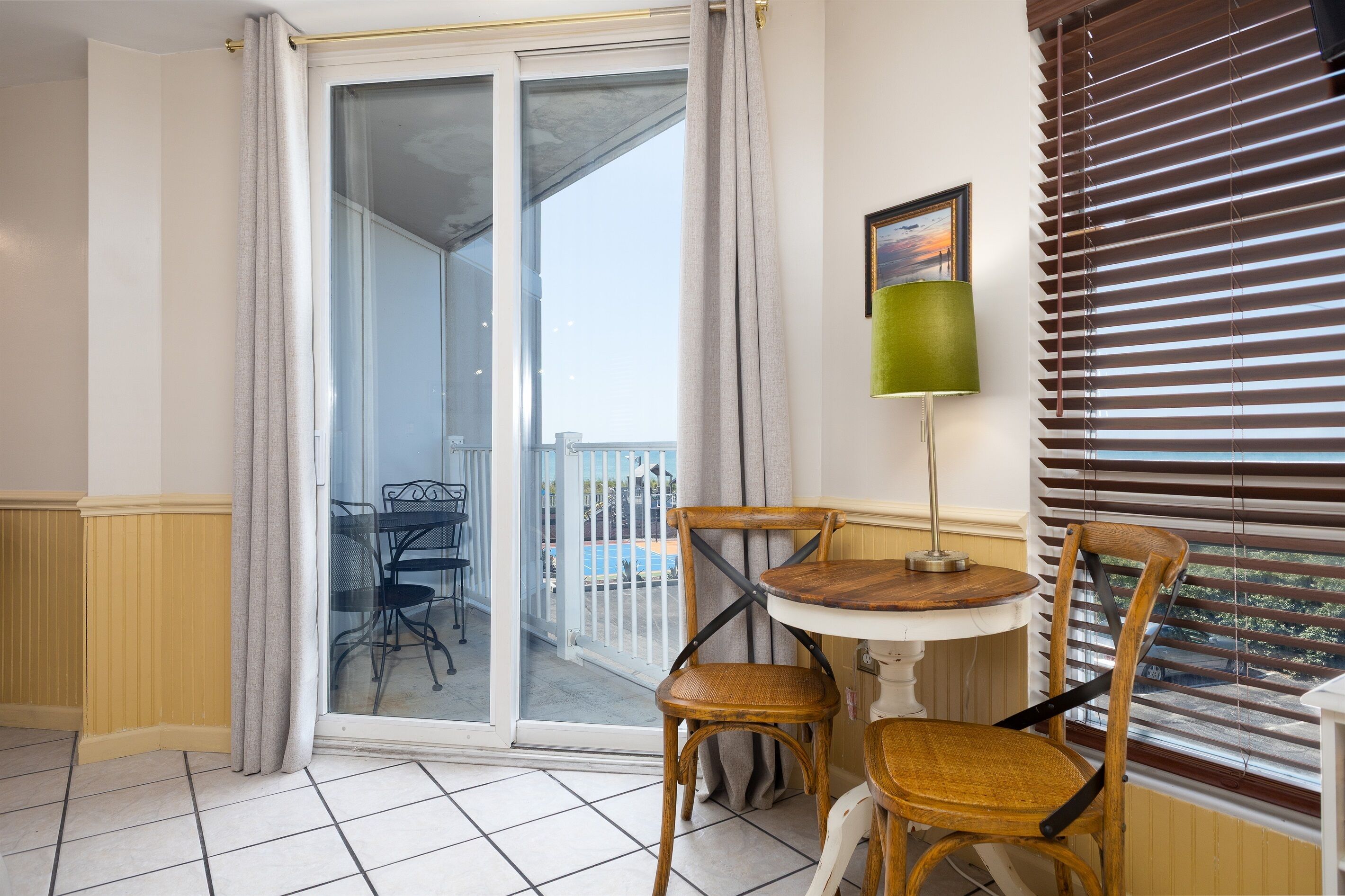 A balcony with a sliding glass door, a table with chairs, and a view of a swimming pool.
