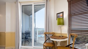 Un balcón con puerta corredera de vidrio, una mesa con sillas y vista a una piscina.