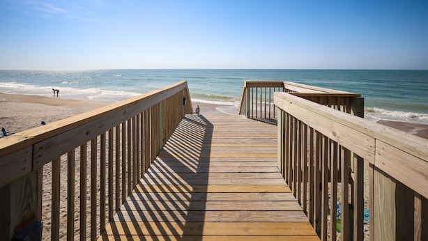 Un paseo marítimo de madera que conduce a una playa con cielos despejados.