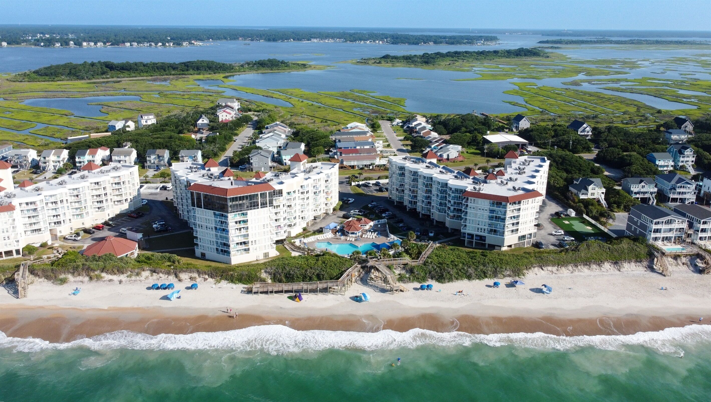 A coastal resort with beachfront villas, a swimming pool, and a beach with umbrellas.