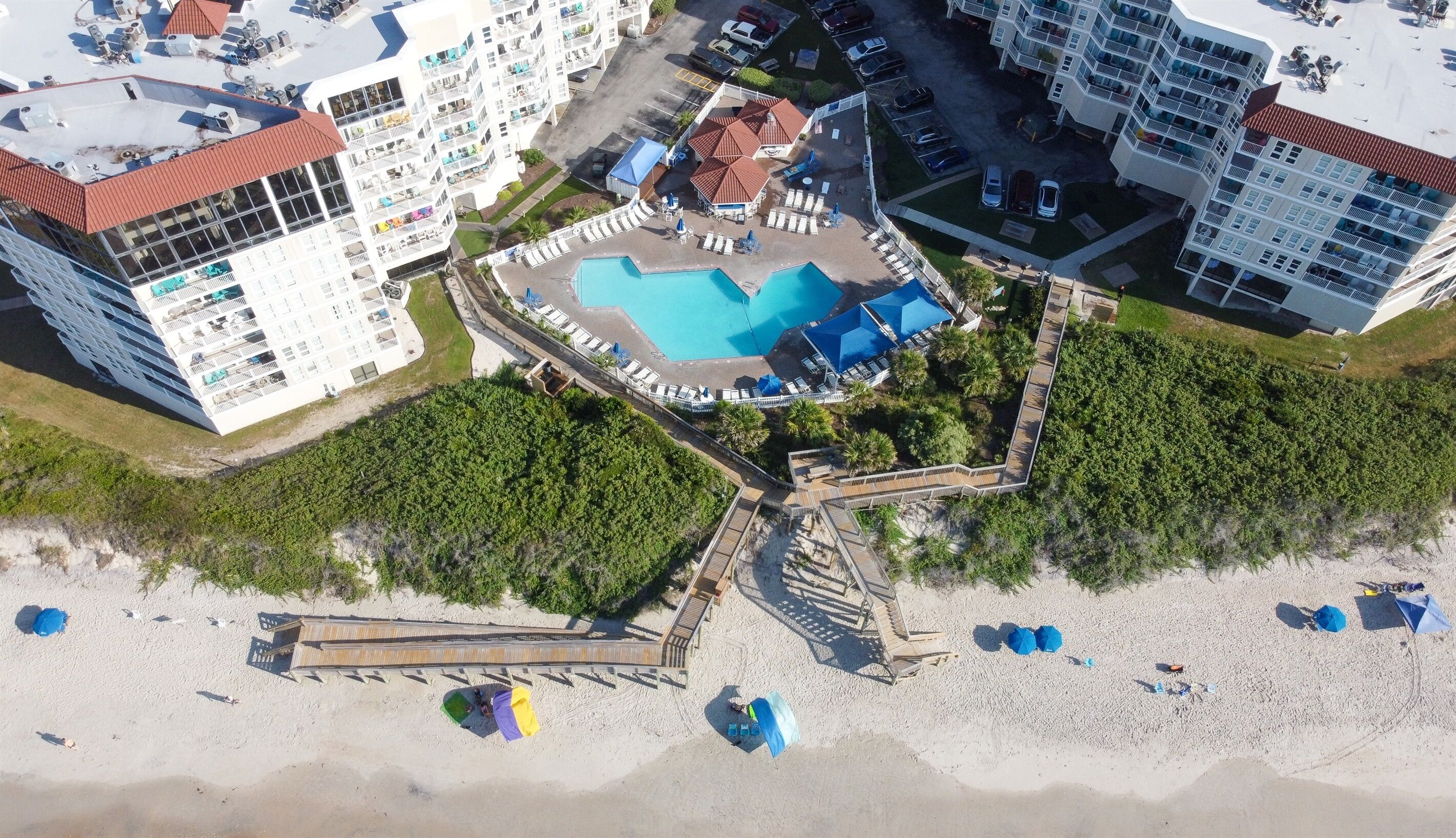 An aerial view of a resort with multiple buildings, a central swimming pool, and a beach area.