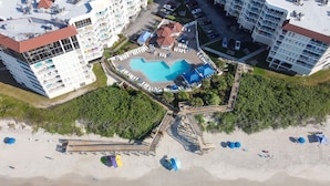Vista aérea de un complejo turístico con varias edificaciones, una piscina central y una zona de playa.