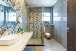 Un baño moderno con ducha de vidrio, un lavabo grande y blanco, y un inodoro.