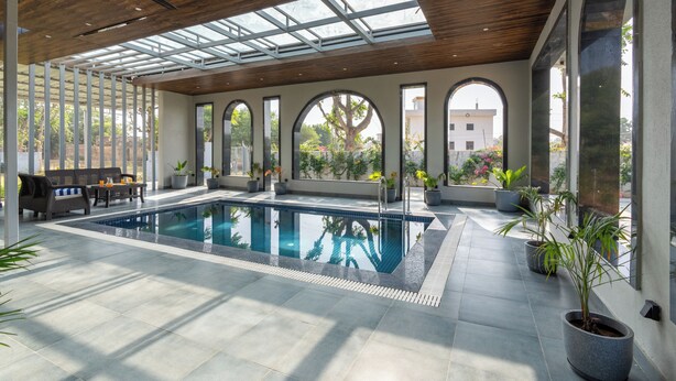 Un área de piscina interior moderna con techo de madera, ventanas amplias y plantas en macetas.