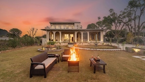 Una casa moderna con una fogata en el jardín, muebles de exterior y un jardín bien cuidado.
