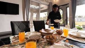 Una mesa de desayuno con diferentes platos, un televisor montado en la pared y vistas al exterior.