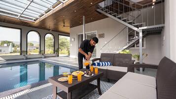 A poolside area with a dining table set with food and drinks, a sofa, and a staircase leading to an upper level.