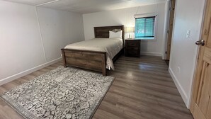 Une chambre à coucher comprenant un lit, une table de chevet, une lampe, une fenêtre et un tapis à motifs.