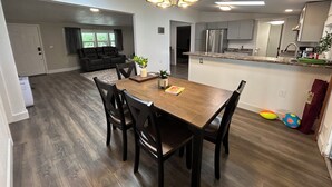 Une cuisine moderne dotée d’un îlot central, un coin repas avec une table et des chaises en bois, et un salon avec un canapé de couleur sombre.