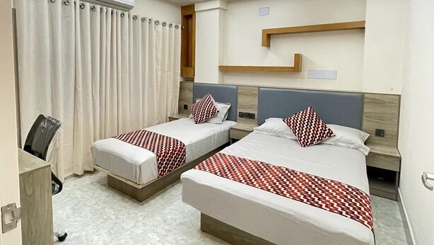 A hotel room with two beds, a ceiling fan, an air conditioning unit, a window with curtains, and a wooden headboard. - The Asteria Hotel Bogura (Bogra)