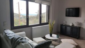 A modern living room with a large window, a sofa, a small round table, and a cabinet.