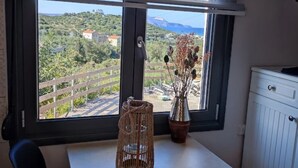 A room with a large window overlooking a scenic landscape, a wicker basket, and a vase with dried flowers.