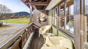 A wooden porch with wicker furniture, a hanging planter, and a view of a green landscape.