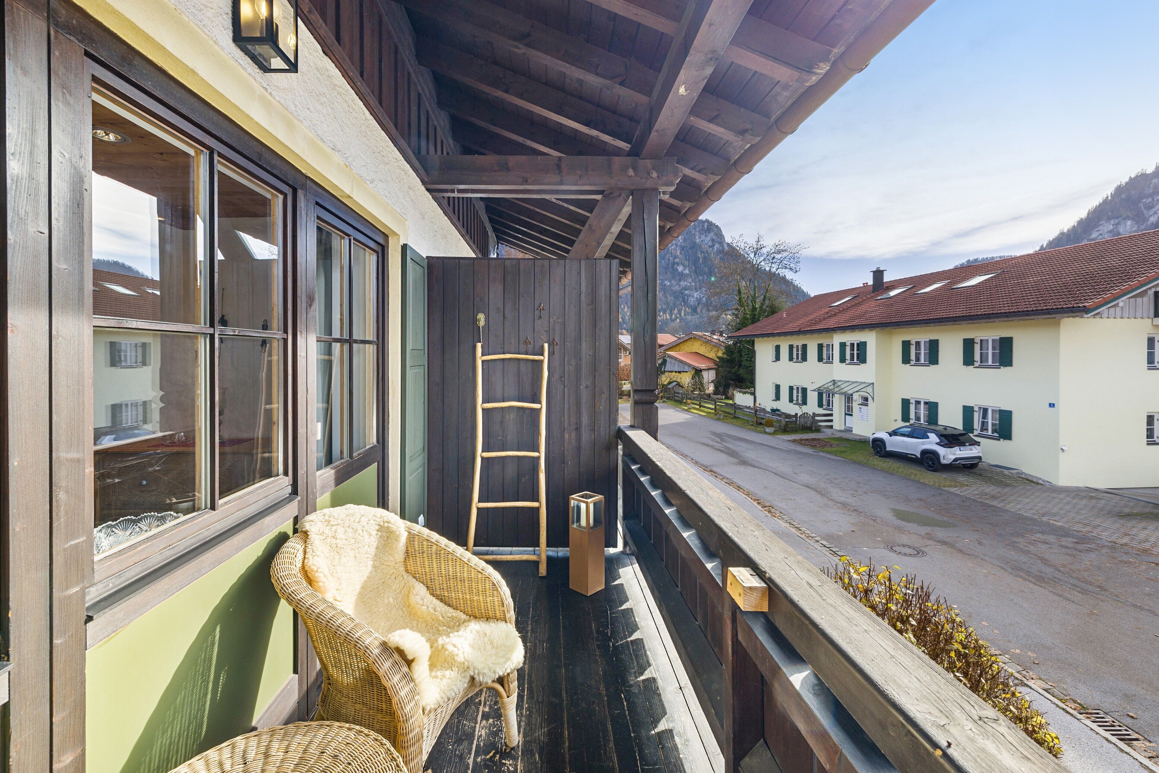 Ein Balkon mit Korbstühlen, einer Leiter und Blick auf eine Straße mit Häusern und einem Berg.