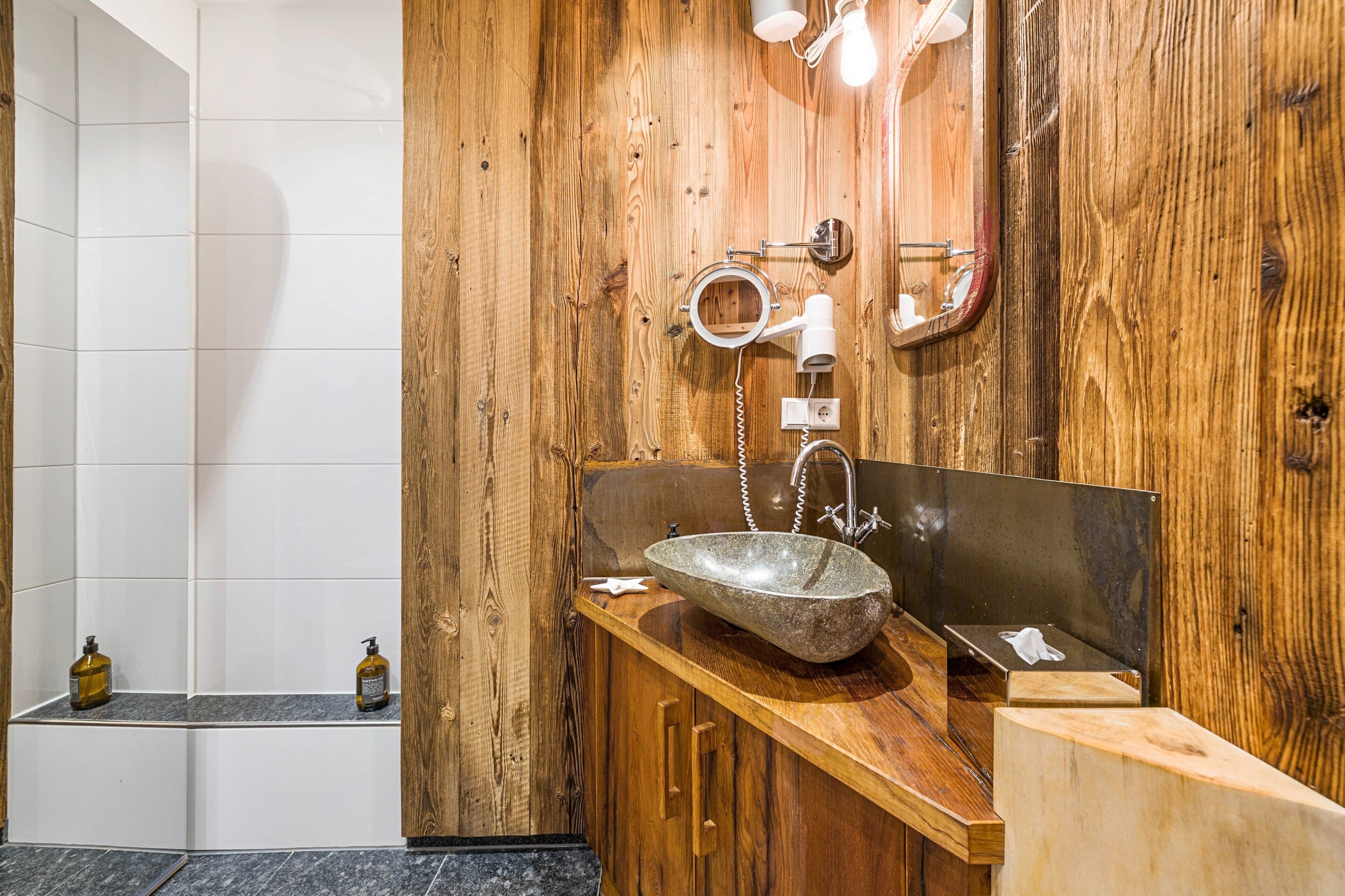 A wooden vanity with a stone sink, a mirror, and a towel dispenser.