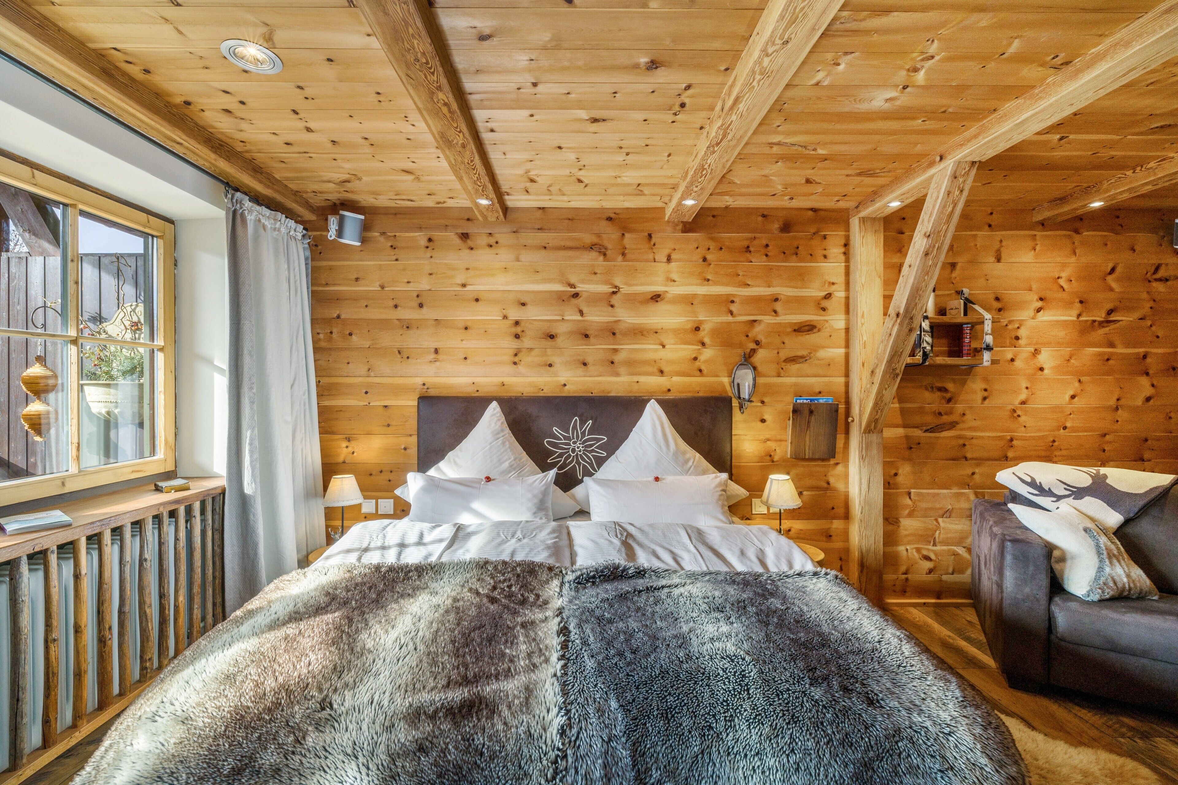 A wooden cabin room with a bed, a sofa, a window, and a wall-mounted shelf.