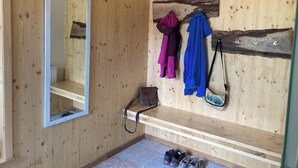 Une pièce en bois, avec un miroir, un banc et un porte-manteau mural où sont accrochées deux vestes.