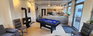 A pool table in a modern living room with a fireplace, comfortable seating, and a kitchen in the background.