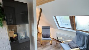 Ein Loft-Zimmer mit Holzbalkendecke, Kamin, Oberlicht und einer Sitzecke mit Sessel und Sofa.
