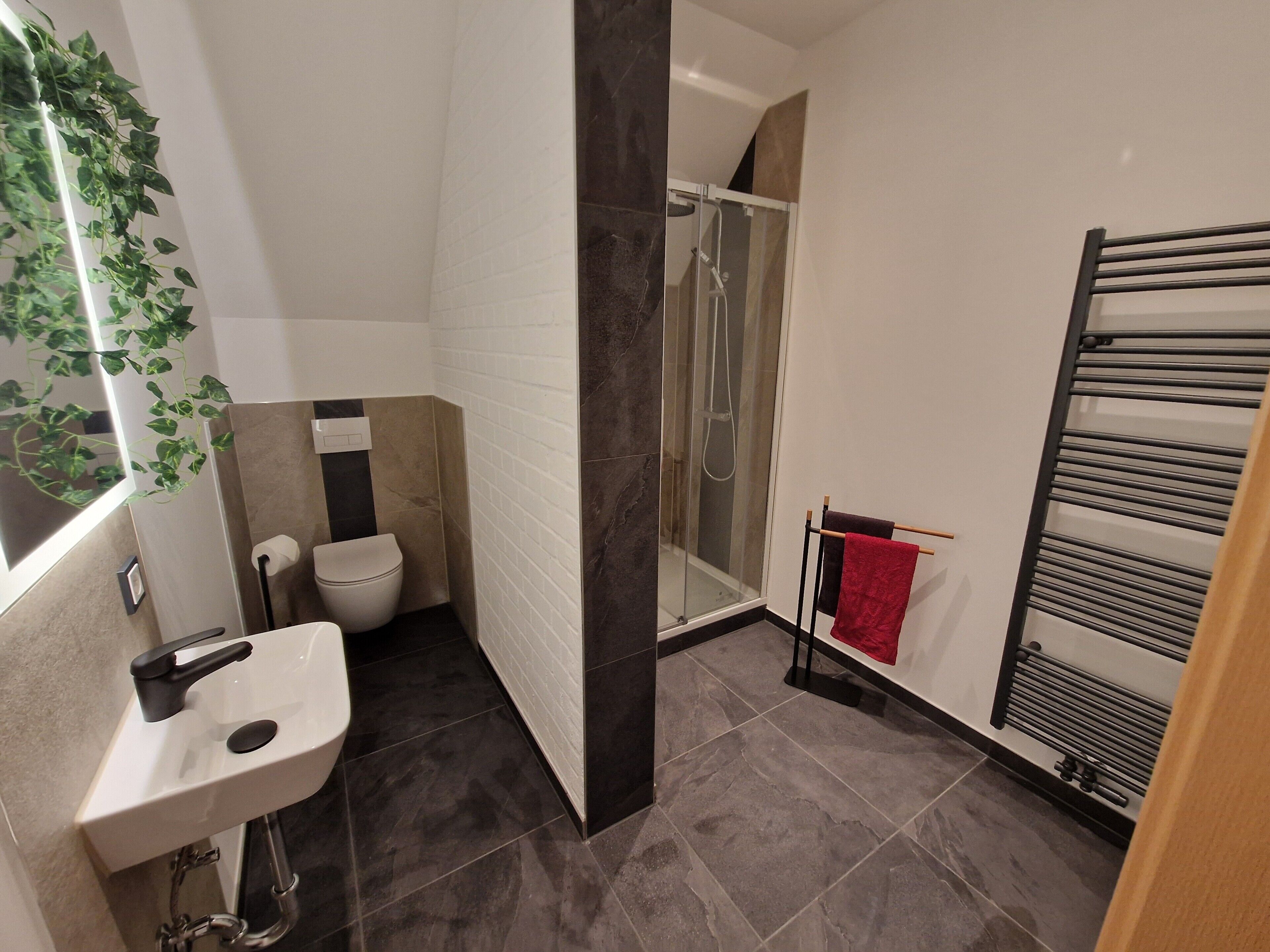 A bathroom with a shower, toilet, sink, and towel rack.