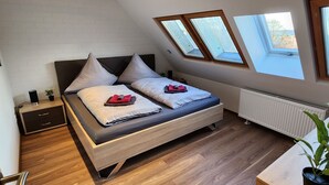 Ein Schlafzimmer mit Schlafplatz in der Schräge, einem Fenster, einer Heizung, einem Schreibtisch und einer Pflanze.